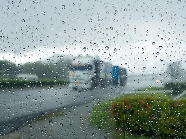 Regenwassertropfen auf Spiegelwand nach Regen mit verschwommenem LKW, der auf der Straße fährt und frischem Grün am Wegesrand im Hintergrund. Sicherheit im Straßenverkehr bei Regen. — Stockfoto