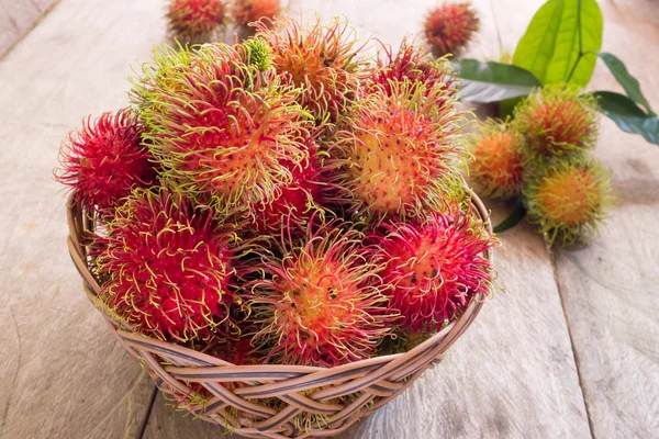 Rambutan rojo fresco dulce deliciosa fruta en cesta en la mesa de madera. Árbol frutal tropical, nativo del sudeste asiático, cultivado en muchos países de la región . — Foto de Stock