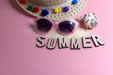 Yaz arkaplanı, güneş gözlüğü, kum ve hasır şapkalı pembe masa.