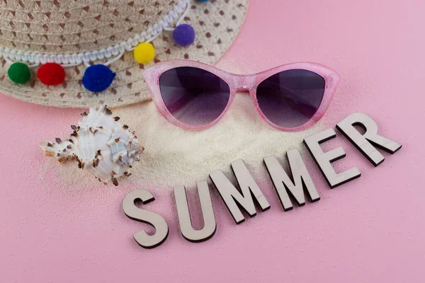 Yaz arkaplanı, güneş gözlüğü, kum ve hasır şapkalı pembe masa.