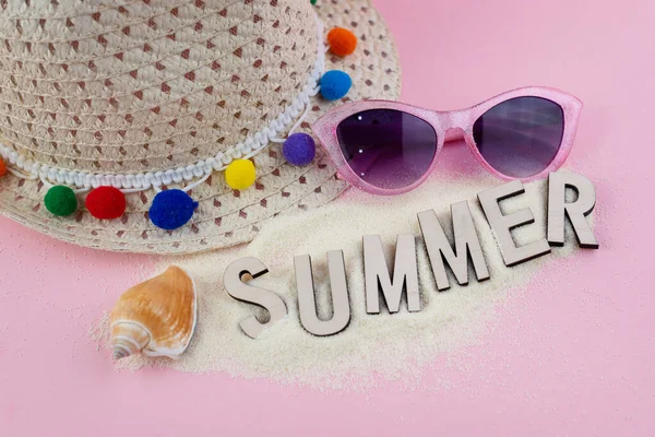 Yaz arkaplanı, güneş gözlüğü, kum ve hasır şapkalı pembe masa.