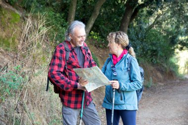 Üst düzey bir çift aktif emekliliklerinin tadını çıkarıyor, bir harita ve yürüyüş kutuplarıyla bir orman yolunda yol alıyorlar, açık havada keşif ve iletişim anlarını paylaşıyorlar.