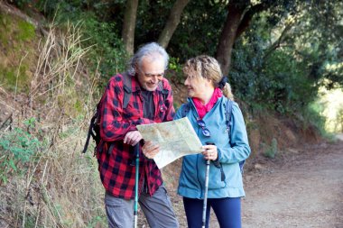 Yaşlı çift ormanda yürürken doğanın tadını çıkarıyor, birlikte haritaya bakıyor ve bir sonraki yollarını planlıyorlar, sağlıklı ve aktif yaşam tarzlarını gösteriyorlar.