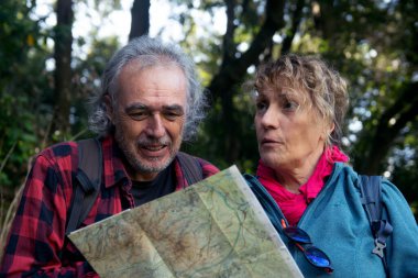 Üst düzey bir çift ormanda yürüyüş yapıyor, kağıt bir haritaya aktif olarak danışıyor ve yönleri tartışıyor, macerayı, keşfi ve doğada birlikte yollarını bulmayı temsil ediyorlar.