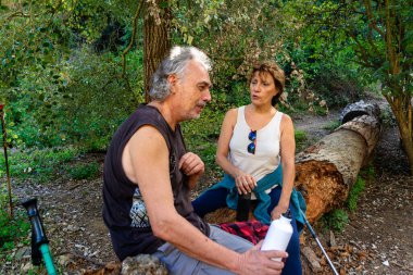 Kıdemli çift düşmüş bir kütükte oturuyor, yürüyüşe ara veriyor, sohbet ediyor, yemyeşil orman ortamında aktif ve sağlıklı kalıyorlar.