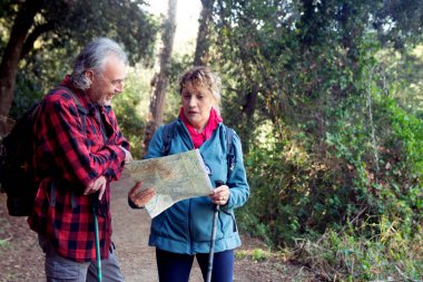 Üst düzey bir çift ormanda yürüyüş yapıyor, kağıt haritaya bakmak için kirli bir yolda duruyor, maceraları sırasında açık hava keşifleri ve takım çalışmalarından zevk alıyorlar.