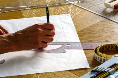 Kadın eli, bant ve aletlerle çevrili beyaz kağıt üzerine bir kıyafet deseni çizmek için kalem ve cetvel kullanır.