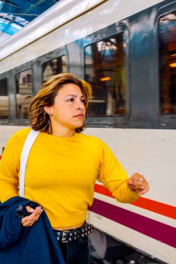 Sarı kazaklı ve siyah kotlu genç bir kadın trenin yanında koşuyor, iş seyahatinde, seyahatinde, seyahatinde ya da acil bir varış noktasında.