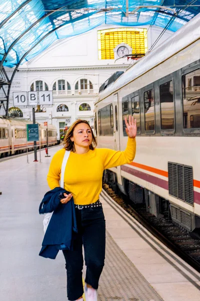 Genç bir kadın trene biniyor, bir platformda duruyor ve el sallıyor, seyahat, kalkış, yolculuk ve yoğun bir tren istasyonundan yeni başlangıçları temsil ediyor.