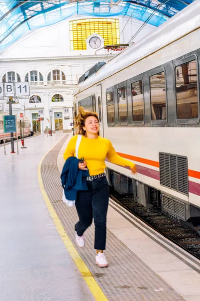 Tren peronunda aceleyle koşan genç bir kadın, istasyondan ayrılan trenini yakalamaya çalışıyor, aciliyet ve seyahat gecikmeleri kavramını gösteriyor.