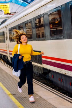 Tren istasyonunda mutlu bir şekilde koşan genç bir kadın, saçları uçuşan, sabit bir trenin yanından aceleyle geçerken, seyahat ve seyahat ile seyahat arasındaki yoğun duyguyu yakalıyor.