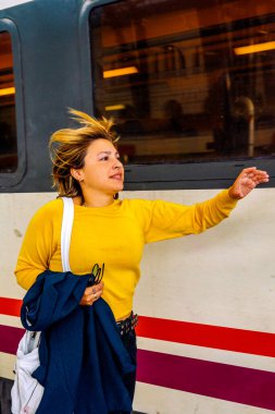 İstasyondaki genç kadın tren hareket ederken el sallıyor, rüzgar saçlarını dalgalandırıyor veda, hareket, umut ve günlük yolculuğunu yakalıyor.