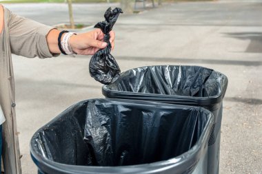 İnsanlar, içinde evcil hayvan atıkları olan siyah bir çantayı siyah bir torbayla halka açık bir çöp kutusuna atıyorlar. Bu da sorumlu hayvan sahipliğini ve şehir hijyenini gösteriyor.