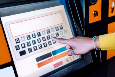 Genç kadınlar, bir şehir tren istasyonunda bir self servis bilet makinesinin dokunmatik ekran qwerty klavyesinde el yazıları yazıları yazarlar, bir banliyö yolculuğu için seyahat seçenekleri seçerler.