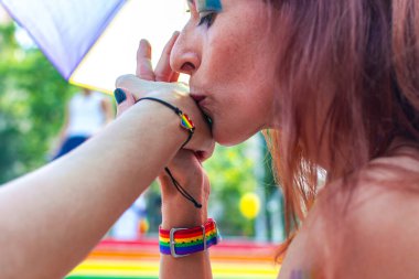 Bir kadın başka bir insanın elini öpüyor, lgbtq artı topluluğunun çeşitliliği ve dahil edilmesi için sevgi ve gurur gösteriyor, gökkuşağı bayrağı desenli aksesuarlar takıyor