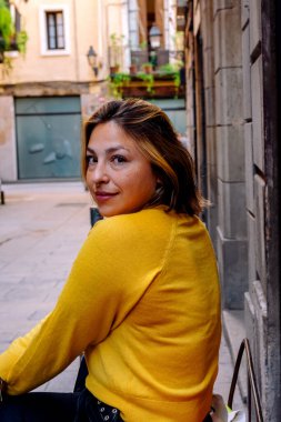 Parlak sarı kazaklı genç kadın arkasını dönüp gülümseyerek büyüleyici bir Avrupa kaldırım taşından sokak arasında dolaşırken gündüz keşfinden ve rahat yalnız seyahat hislerinden keyif alıyor.