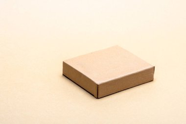 Minimalist açık bej bir zemin üzerinde oturan boş dikdörtgen kahverengi karton kutu, çeşitli işletmeler için taşımacılık, teslimat, ambalaj ve e ticaret sembolize