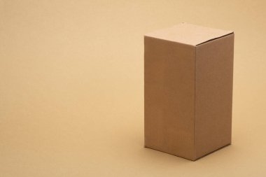 Brown corrugated carton packaging box in a vertical orientation against a neutral beige background, representing delivery, shipping, and storage concepts in e commerce and logistics
