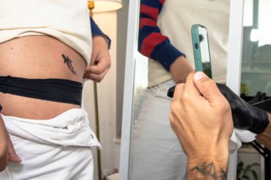 Kalçasında yeni mürekkeplenmiş bir köpekbalığı vücut sanatını belgeleyen kişi, yaratıcı ifadesini ve kişisel tarzını stüdyoda akıllı bir telefonla yakalıyor.