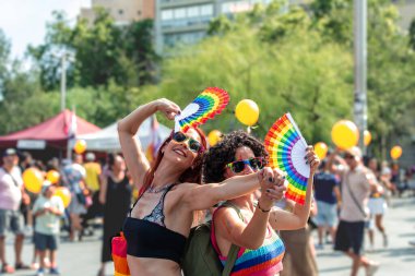 Neşeli iki kadın, renkli gökkuşağı hayranları olan ve neşeli kalabalığın arasında uyumlu güneş gözlüğü takan bir geçit törenine neşeyle katılıyorlar.
