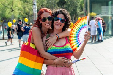 Gökkuşağı aksesuarları giyip kucaklaşan, atmosferin tadını çıkaran, çeşitliliği, kapsamı ve aşkı coşkulu bir lgbtq artı gurur etkinliğinde kutlayan iki kadın.