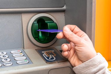 Mor plastik kartı otomatik veznedar makinesine yerleştiren kişinin eli. ATM makinası, finansal yönetim ve nakit erişimi için bir banka işlemi yapıyor.