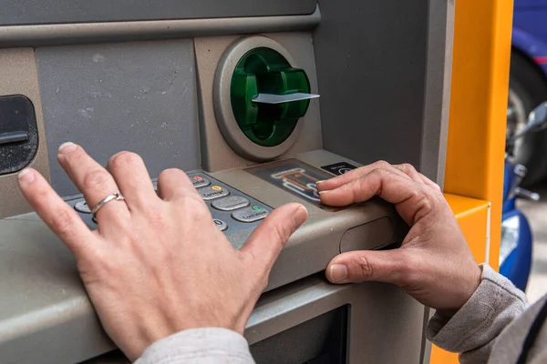 Otomatik veznedara erişmek için kredi kartı kullanan bir kişi, bir caddedeki banka hesabından para çekmek için finansal işlem yapıyor.