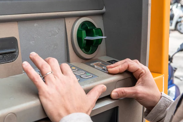 Kişinin elleri otomatik veznedar makinesiyle etkileşime giriyor, kredi kartını yuvaya sokuyor, bu sırada tuş takımına bir pim takıyor ve banka işlemini tamamlıyor.