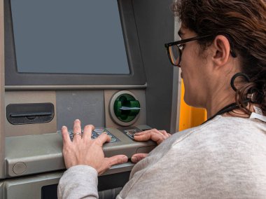 Para transferi için para makinesini kullanan bir kadın gizli şifresini tuş takımına girerek para çekme işlemi sırasında güvenliği ve mahremiyeti öncelik haline getiriyor.