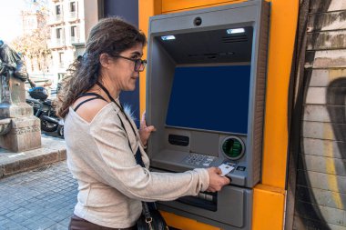 Otomatik veznedarın önünde duran bir kadın, kredi kartını işleme sokup şehirdeki bir caddedeki banka hesabından para çekiyor.