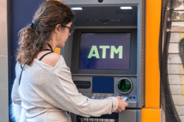 Kadın açık hava veznedar makinesine banka kartı sokuyor, para çekme ya da sokakta denge soruşturması gibi finansal işlemler yapıyor.