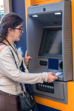 Gözlüklü bir kadın şehirdeki bir bankamatiğe kredi kartı yerleştiriyor. Her gün para çekmek için banka işlemleri yapıyor.