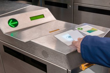 Çağdaş metalik toplu taşıma turnikesi okuyucusuna yeşil ok göstergesi ile beyaz bir rFID kartı takan kişi, otomatik bariyerden geçişi sağlıyor.
