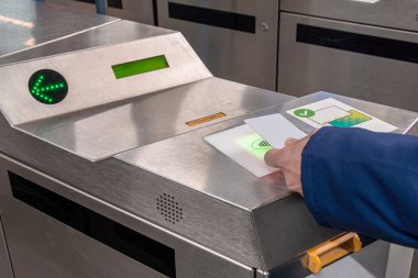 Bir toplu taşıma turnikesinin aydınlatılmış okuyucusuna beyaz bir RFID kartı tutarak metro ya da metro sistemine giriş için irtibatsız ödeme olanağı sağlıyor.