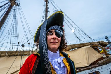 Eski gemi güvertesinde dikilen kadın, korsan kostümü giymiş, üç mısır şapkası, göz bandı ve bandana takmış, heyecanlı bir festival sırasında macera ve özgürlüğü somutlaştırıyor.