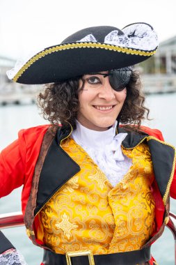 Bir kadın gülümsüyor ve bir göz bandı, fırfırlı gömlek ve bir tricorn şapka ile tarihsel bir korsan kaptanı kostümü giyiyor, temalı bir etkinlik veya karnaval keyfini çıkarıyor.
