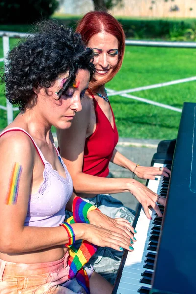 Tenlerinde gökkuşağı renkleri olan ve gökkuşağı aksesuarları takan iki kadın açık havada piyano çalıyor, gey gururunu kutluyor ve müziğe olan sevgilerini ifade ediyorlar.