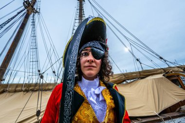 Eski bir yelkenli güvertesinde üç mısır şapkalı ve göz bantlı kadın korsan, kırmızı ceket ve altın yelek, donanım ve deniz altının ortasında kılıç desteği ile karnaval kostümünü kutluyor.