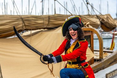 Göz bandı takmış ve şapkalı bir kadın marinada canlı bir karnaval kutlamasında elinde kılıçla güvertede gülümsüyor, neşeli bir kostüm ve neşeli bir poz.