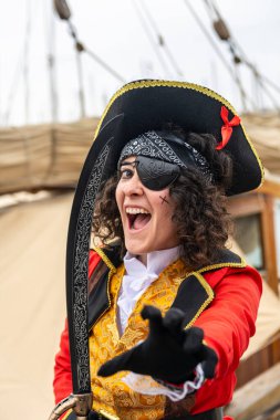 Karnaval kostümlü, göz bandı ve trikorne şapkalı kadın korsan kaptan, elinde kılıç, güvertede şakacı, maceraperest bir açık hava gösterisinde kostümlü resim.