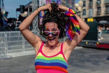 Canlı gökkuşağı çizgili, güneş gözlüklü ve yüz boyalı bir bluz giyen, çeşitliliği etkin bir şekilde kucaklayan ve lgbtq artı gururu kutlayan biri.