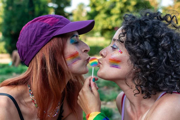 Gökkuşağı makyajı ve makyajlı iki kadın gökkuşağı lolipopunu öpüyor. Aşkı, çeşitliliği ve Igbtq 'ı temsil ediyor.