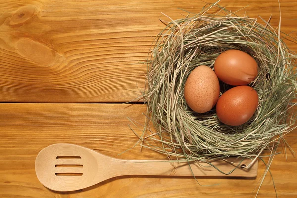 La composición de tres huevos de pollo en un nido de hierba y cuchara de madera acostado en un panel de tableros marrones vintage con espacio libre para la publicidad de texto de la comida o el diseño de menú de restaurante . — Foto de Stock