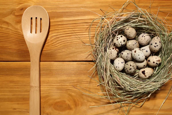 La composición de huevos de codorniz en un nido de hierba y cuchara de madera acostado en un panel de tableros marrones vintage con espacio libre para la publicidad de texto de la comida o el diseño de menú de restaurante . — Foto de Stock