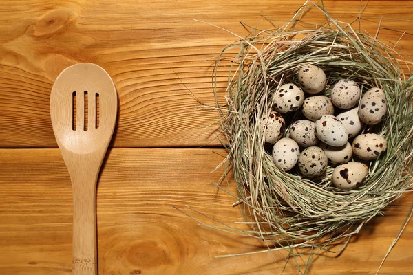 La composizione di uova di quaglia in un nido da erba e cucchiaio di legno sdraiato su un pannello di tavole marroni vintage con spazio libero per la pubblicità di testo di cibo o ristorante menu design . — Foto Stock