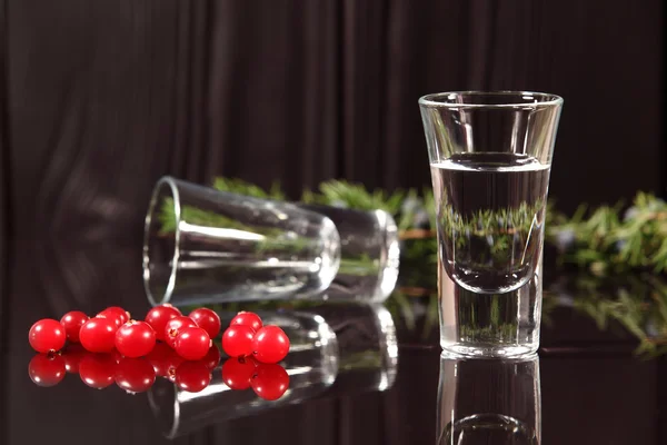 Komposition aus zwei Gläsern mit Alkohol und roten Beeren Preiselbeeren, die auf einer glänzend schwarzen Oberfläche auf einem Hintergrund aus alten Holzbrettern stehen. Selektiver Fokus — Stockfoto