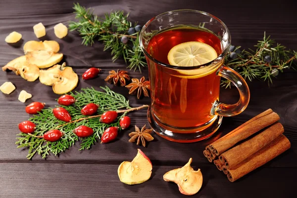 A cup of hot tea with lemon on a rustic table from textured vintage boards. Next to them are berry dog-rose, the fruit of anise, cinnamon sticks, dried apples and juniper twig. Selective focus