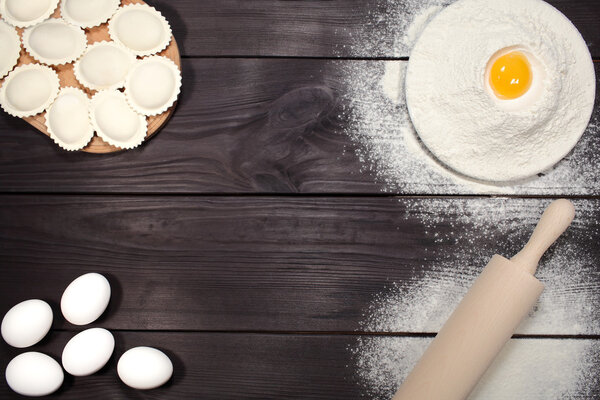 Homemade dumplings near a plate of white flour and kitchen rolling pin lying on an old rustic table. Composition for design culinary recipe or menu