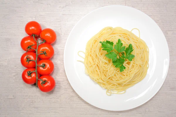 Comida italiana: pasta en un plato blanco grande junto a los tomates cherry rojos y aceitunas verdes —  Fotos de Stock