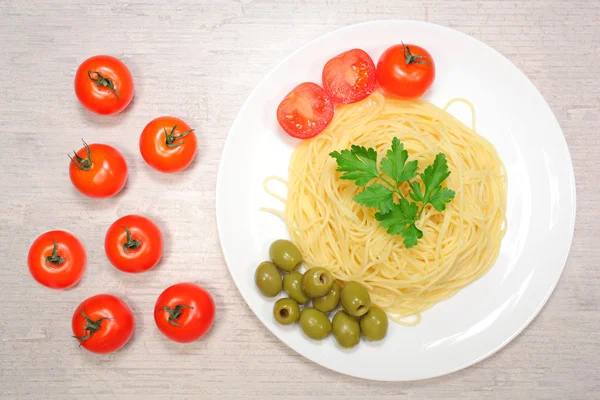 Итальянская еда: макароны на большой белой тарелке рядом с помидорами черри и зелеными оливками — стоковое фото
